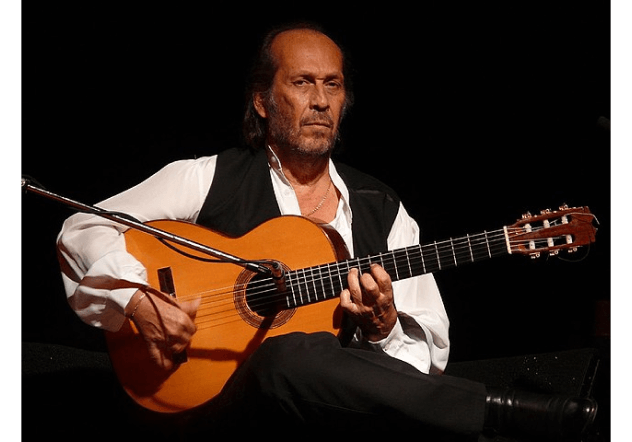 פאקו דה לוסיה יושב על כיסא ומחזיק גיטרה פלמנקו.